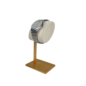 Detail view of gold metal watch stand with soft grey velvet pillow for display