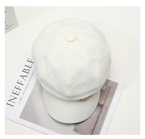 Close-up of cream white newsboy hat showing textured waffle fabric and metal tag detail