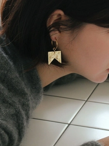 Detailed close-up of gold geometric earrings with square pendants on model's ear
