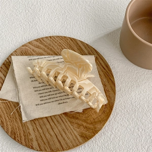 Macro detail of large beige marble acetate hair claw clip on a rustic wooden tray