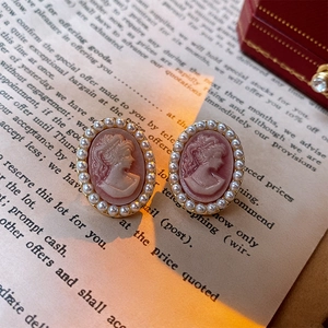 Macro view of vintage cameo earrings with pink portrait and pearl halo on a paper background