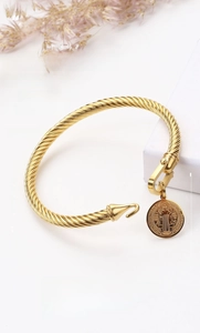 Detailed macro view of gold titanium steel twisted cable bangle with Saint Benedict medal
