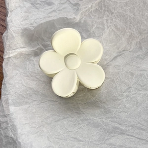 Top view of a matte cream-white flower claw clip on textured white paper background
