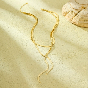 Detail of a gold double-layer snake bone necklace with adjustable clasp on a stone surface