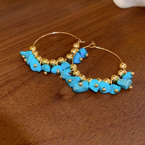 Detailed view of bohemian hoop earrings with blue turquoise stones on a dark wooden surface