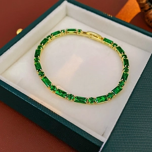 Detalle de pulsera bañada en oro con circón verde esmeralda en una caja de joyas verde