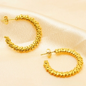 Macro view of gold 18K twisted hoop earrings on elegant champagne silk fabric texture