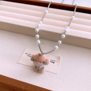 Detailed shot of brown plush dog pendant on pearl beaded necklace over beige jewelry tray
