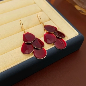 Detail view of burgundy petal tassel earrings with gold hooks on a jewelry box display
