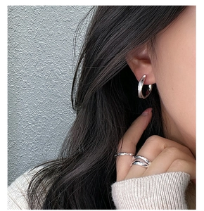 Close-up of elegant silver C-shaped hoop earrings and matching minimalist rings on model