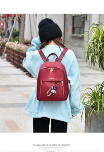 Detail of wine red oxford backpack with gold zippers and panda charm worn by a model outdoors