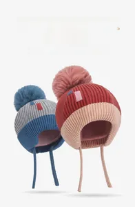 Detail of warm knit baby beanies with large faux fur pom-poms and earflaps in two colors