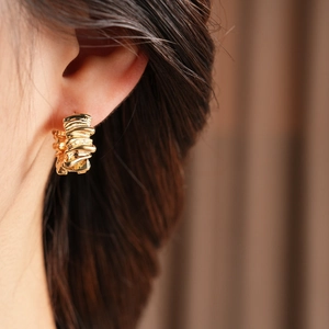 Close-up of golden irregular textured C-shape hoop earring worn by a model