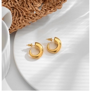 Detailed view of gold hoop earrings with a polished finish on a white ceramic plate