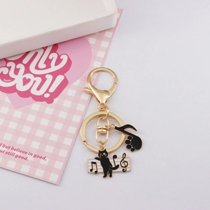 Detailed view of cat and music notes charms on a golden alloy keychain with lobster clasp