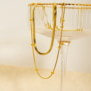 Detail of gold double-layer necklace with snake chain and bead chain on glass