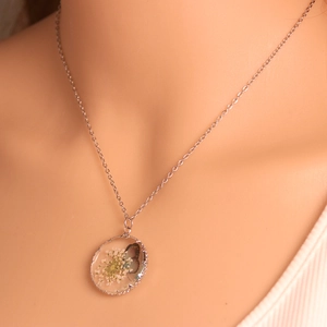 Detailed shot of glass pendant featuring real dried white flowers and butterfly wing