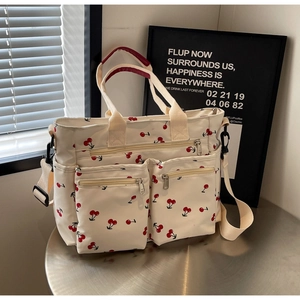 Detail of white nylon tote bag featuring red cherry prints and multi-pocket design on table
