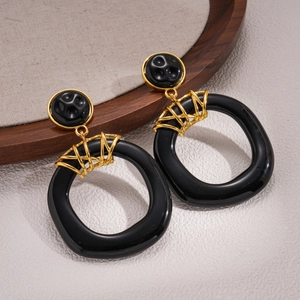 Detailed view of oversized black resin earrings with golden twisted metal wire connection