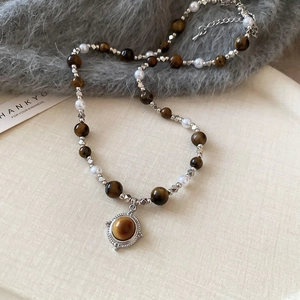 Detailed shot of tiger eye stone and pearl necklace with retro golden pendant on fabric