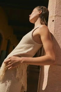 Vista dettagliata del top in maglia beige con lunghe nappe di frange boho laterali