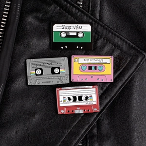 Detail of four retro cassette enamel pins on a black leather jacket with punk vibes