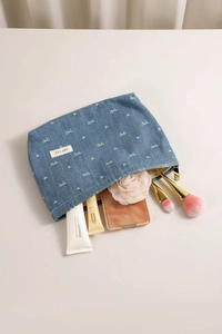 Detail of blue denim cosmetic bag with white bow embroidery and metallic zipper closure