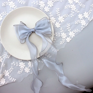 Close-up of grey satin and organza bow hair clip with long ribbons on lace background
