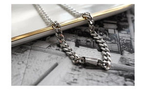 Close-up of silver Cuban link chain bracelet on a vintage plate and newspaper background