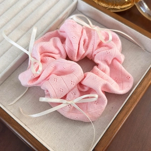 Detailed close-up of a pink ribbed knit scrunchie with a white ribbon bow in a wooden box