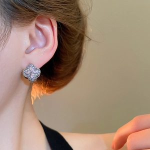 Detailed view of silver clover earrings with sparkling diamonds and purple zircon on ear