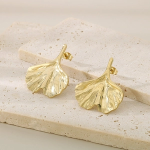 Detailed close-up of golden ginkgo leaf earrings with brushed texture on marble