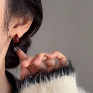 Gros plan de boucles d'oreilles goutte rouge foncé portées avec un pull beige chic