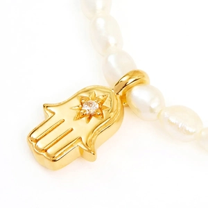 Macro shot of a golden Hamsa hand pendant with star motif on a white pearl necklace
