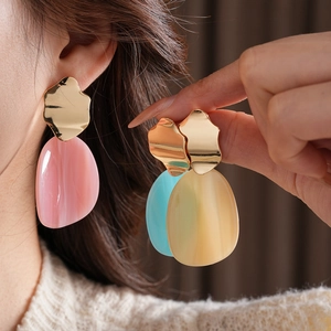Détail de boucles d'oreilles irrégulières en acrylique rose, bleu et beige sur modèle