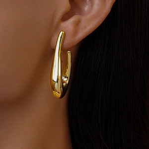 Close-up of golden teardrop hoop earrings featuring a minimalist polished metal finish