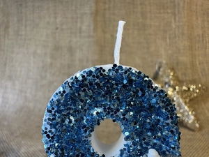 Macro shot of donut-shaped candle with blue sequins and white wick on rustic burlap