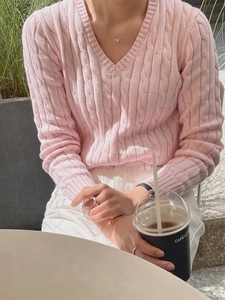 Close-up of pink V-neck cable knit sweater with textured patterns and soft fabric detail