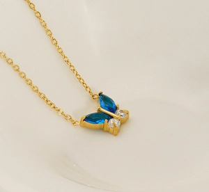 Close-up of golden necklace with blue butterfly pendant featuring zircon stone inlay