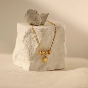 Artistic close-up of golden bow and heart pendant necklace on a decorative stone base