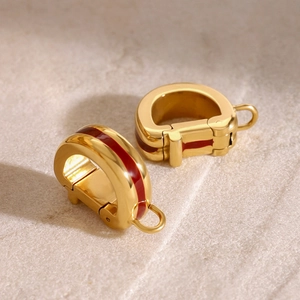 Detailed close-up of C-shaped gold-plated metal earrings with red enamel inlay finish