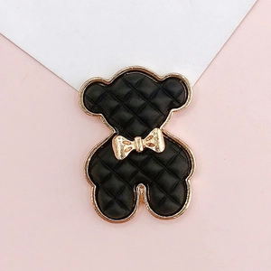Macro detail of a black quilted bear charm with a gold bow and metallic gold border