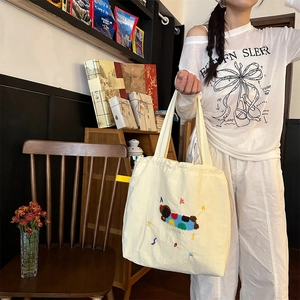 Detail of beige canvas tote with 3D cartoon dog embroidery and yellow side tag
