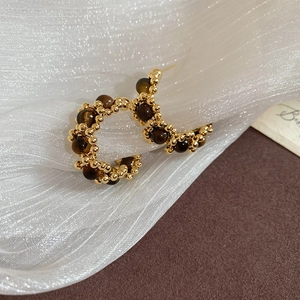 Macro detail of gold C-shaped earrings with tiger eye beads on soft white tulle fabric