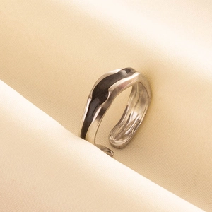 Dettaglio dell'anello a onde d'argento con smalto nero su morbido tessuto beige