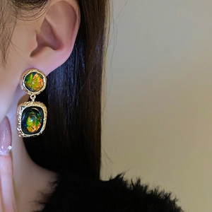 Détail de boucles d'oreilles dorées géométriques avec résine verte et pierre d'opale