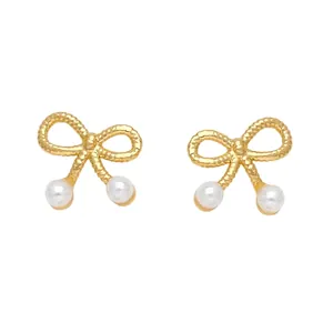 Boucles d'oreilles nœuds dorés avec perles et texture tissée sur un fond blanc épuré
