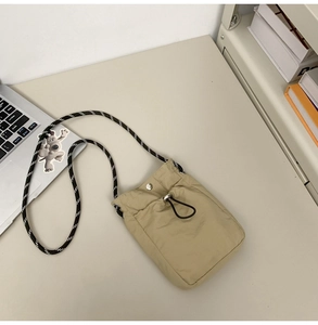 Detail of beige nylon water bottle bag with woven rope strap and drawstring on desk
