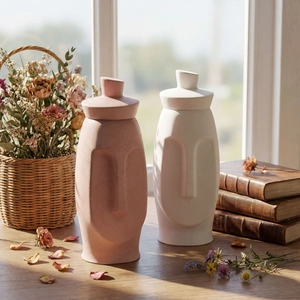 Abstract face-shaped storage jars in pink and white matte ceramic on a wooden table