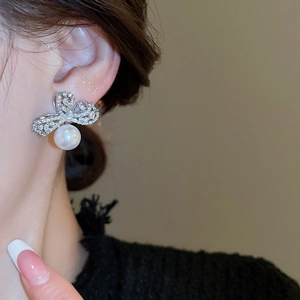 Detail view of silver luxury bow earrings with sparkling cubic zirconia and white pearl drops